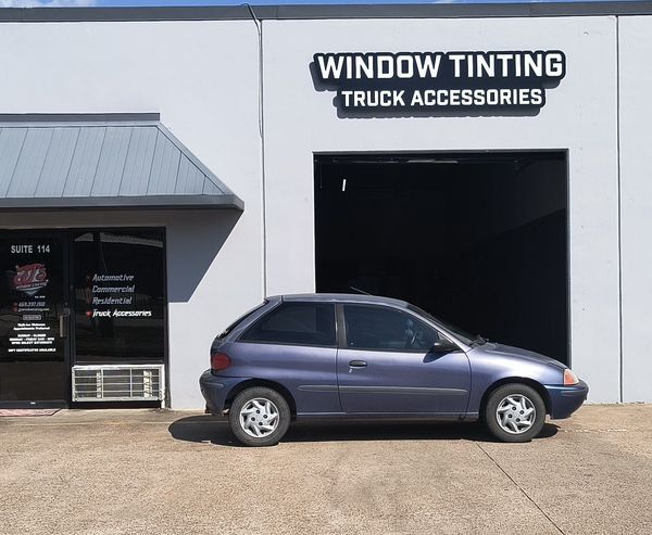 Blue compact car parked outside a window tinting and truck accessories shop.