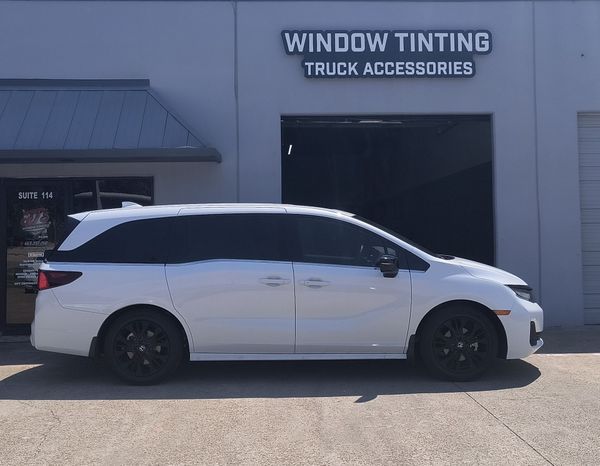 White minivan parked outside a window tinting truck accessories shop.