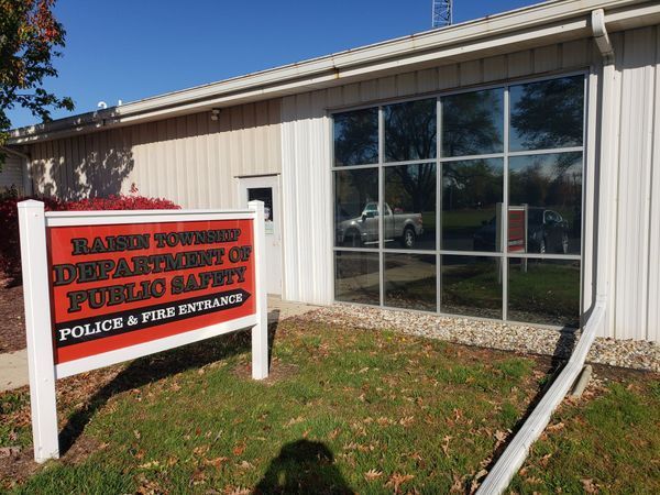 Red-and-black sign for a fire department and public safety building beside a white-sided brick building and windows