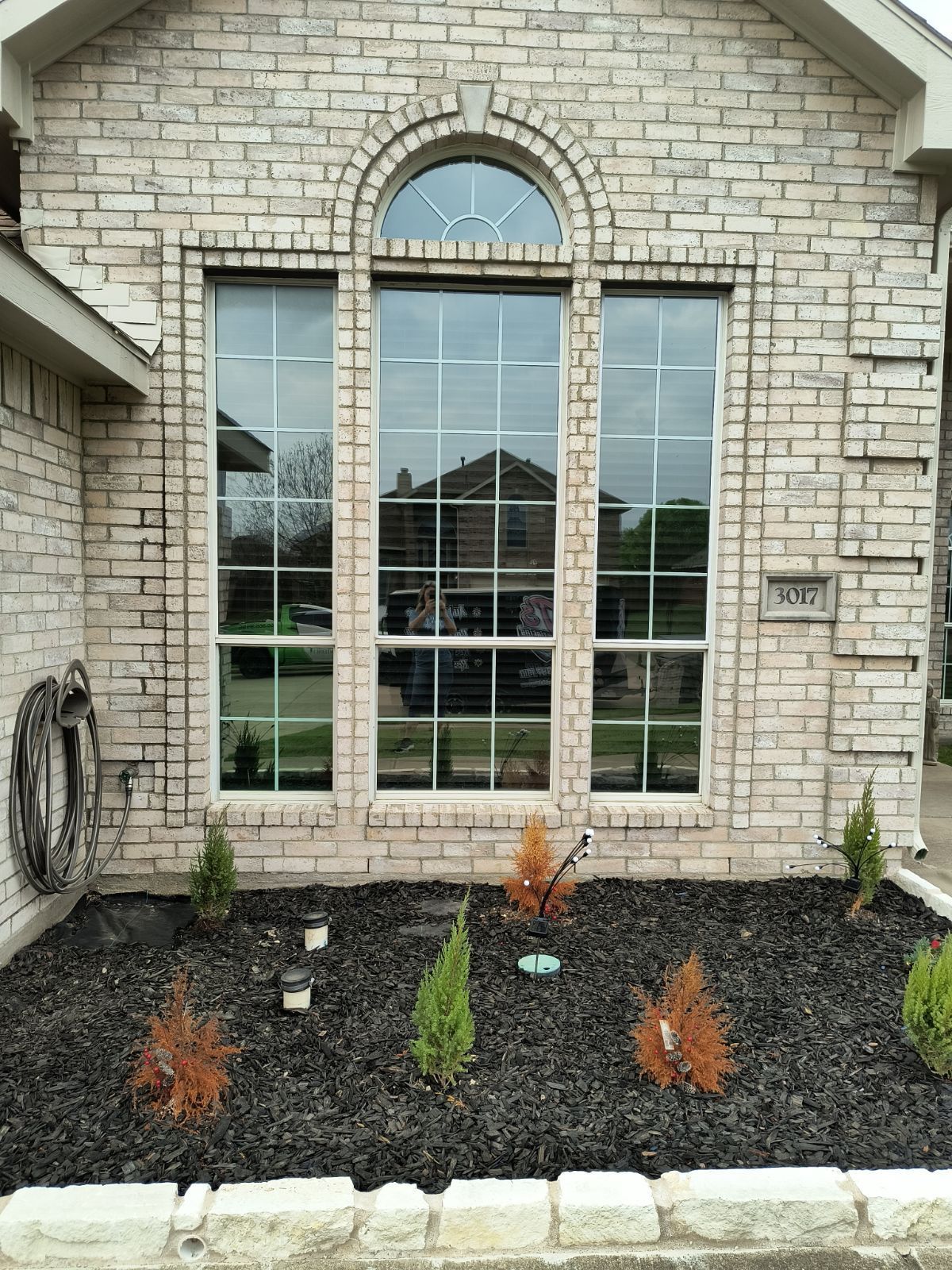 Stone house front with large arched window, small shrubs, and a landscaped garden bed with mulch and rocks