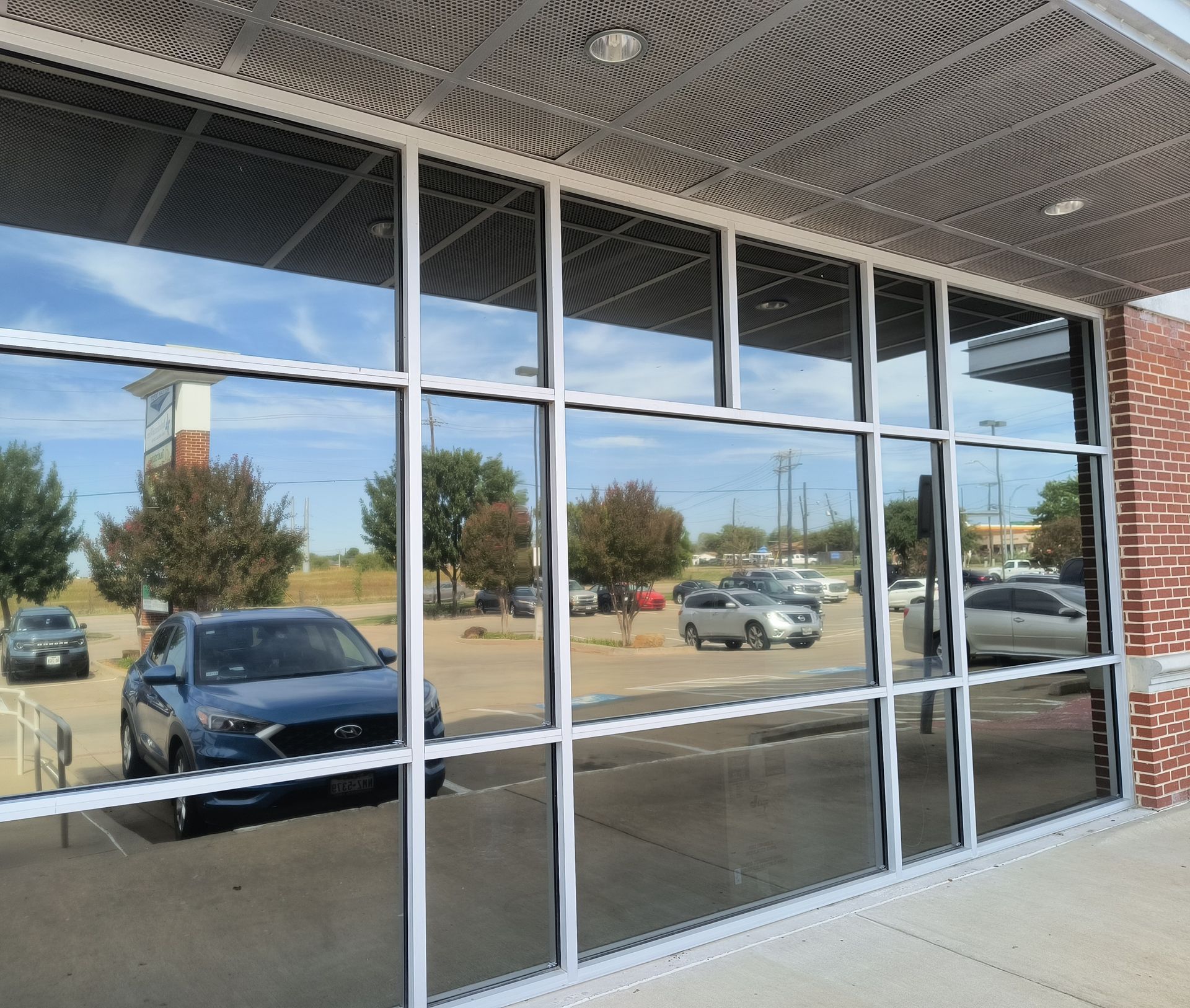 Empty storefront windows reflecting parked cars and a sunny street outside