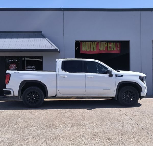 White pickup truck parked outside a building with a yellow “NOW OPEN!” sign in the window