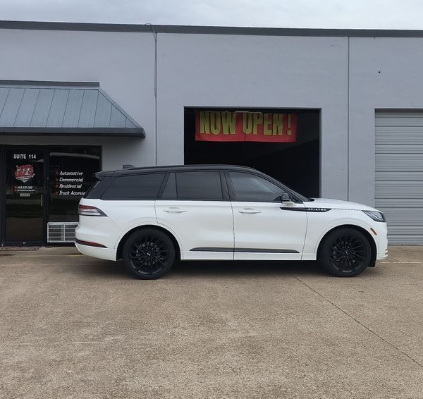 White SUV parked outside a building with a neon “Now Open” sign and closed garage door