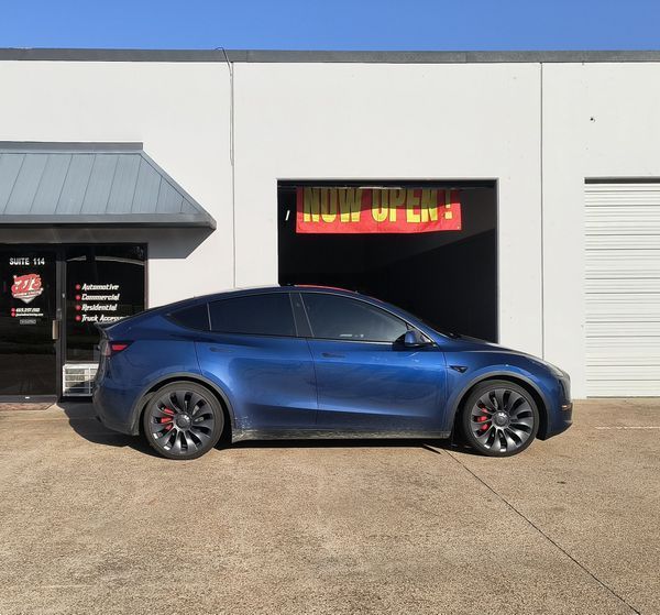 Blue sedan parked outside a building with an open garage door and a colorful sign above it