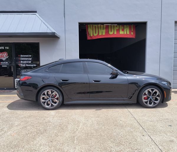 Black sports sedan parked in front of a building with a “Now Open” sign