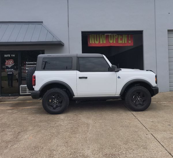 White-and-black two-door SUV parked outside a storefront with a neon “Now Open” sign.