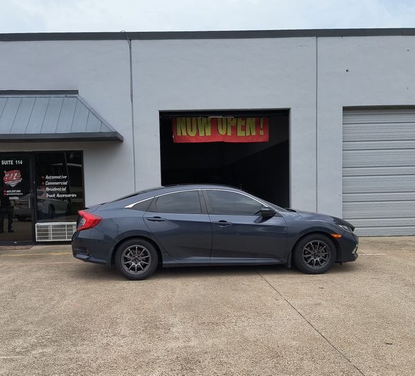 Dark blue sedan parked outside a garage with an open bay and neon sign
