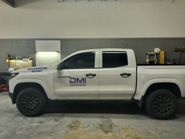 White DMI pickup truck parked indoors in a garage or shop, side view.
