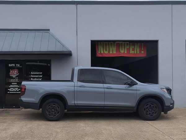 Gray pickup truck parked outside a shop with a red “NOW OPEN” sign in the window.