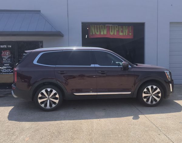 Dark maroon SUV parked in front of a storefront with a neon sign.