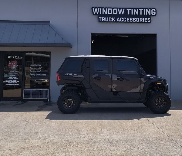 Black off-road SUV parked outside a window tinting and truck accessories shop.