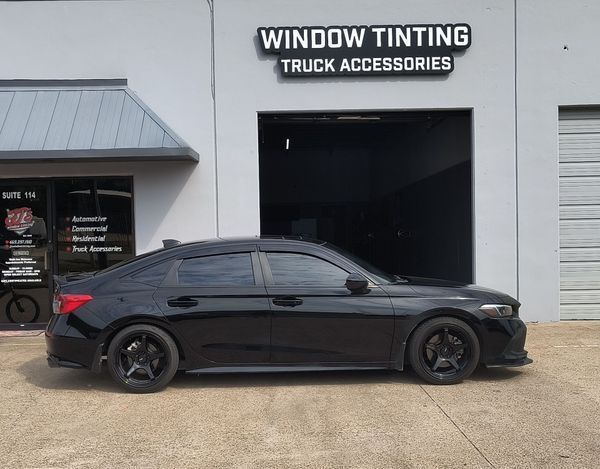 Black sedan parked outside a window tinting and truck accessories shop.