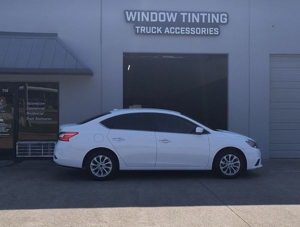 White sedan parked outside a window tinting truck accessories shop.