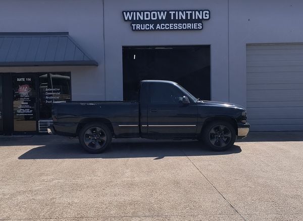 Black pickup truck parked outside a window tinting and truck accessories shop.