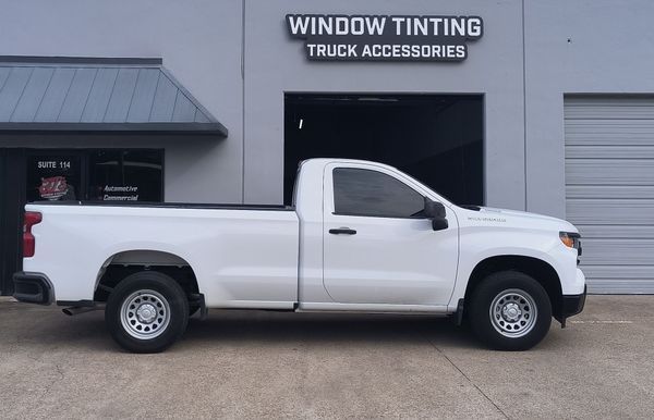 White pickup truck parked outside a window tinting and truck accessories shop.