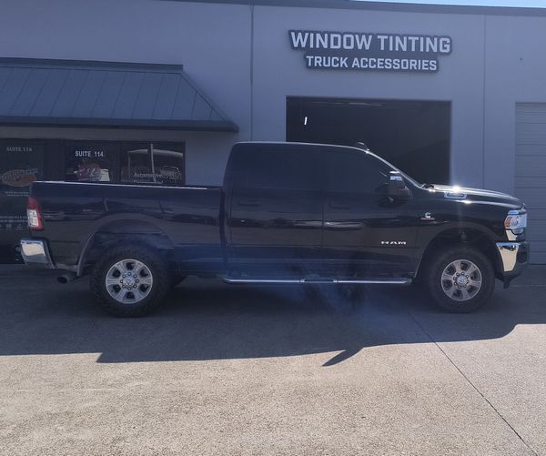Black pickup truck parked outside a window tinting and truck accessories shop.