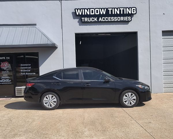 Black sedan parked outside a window tinting and truck accessories shop.