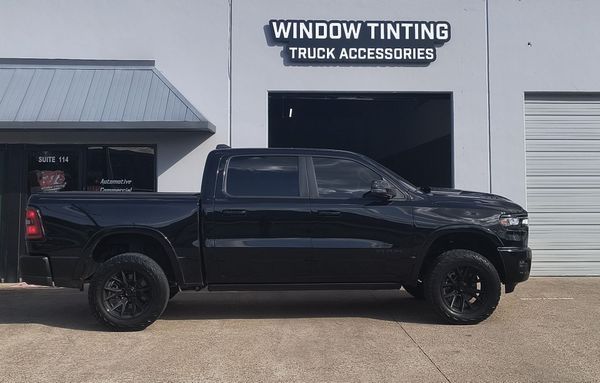 Black pickup truck parked outside a window tinting and truck accessories shop