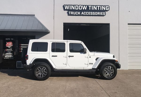 White Jeep Wrangler parked outside a window tinting and truck accessories shop