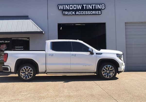 White pickup truck parked outside a window tinting and truck accessories shop.