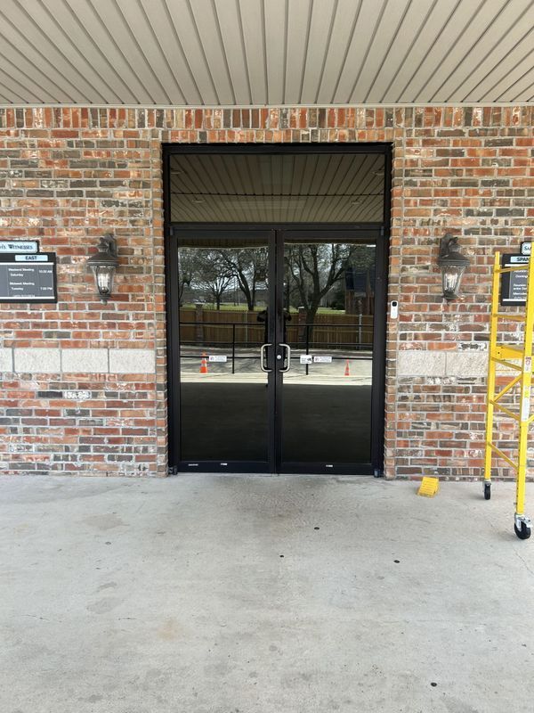 Brick building entrance with black double glass doors and a yellow ladder on the right