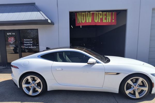 Silver sports car parked outside a building with a red “NOW OPEN!” sign above the garage door