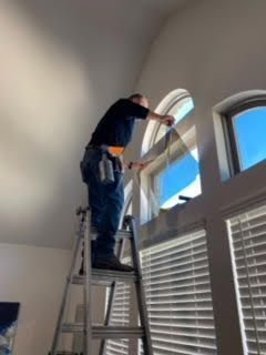 Person on a ladder cleaning an arched window inside a bright room