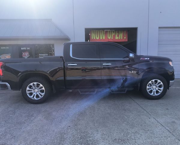 Black pickup truck parked outside a storefront with neon “NOW OPEN” sign.
