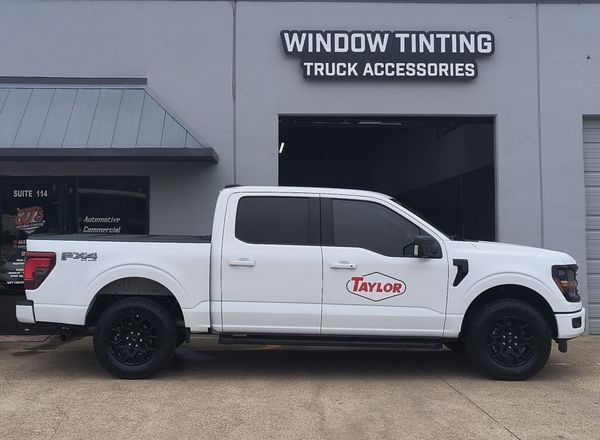 White Ford pickup truck parked outside a window tinting truck accessories shop with a Taylor logo on the door