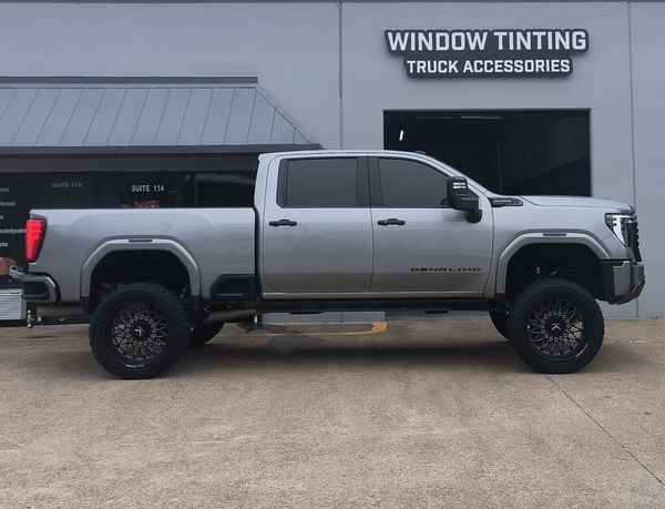 Silver lifted pickup truck parked outside a window tinting and truck accessories shop
