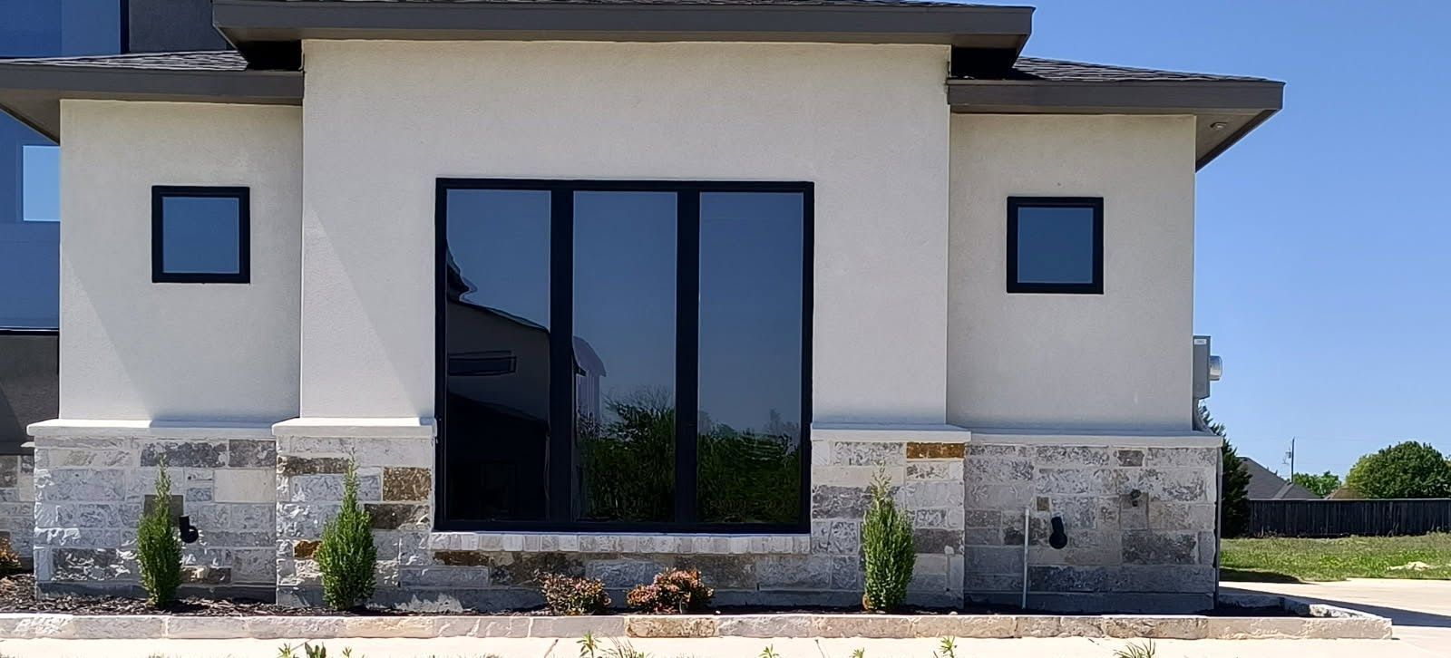 Front view of a modern stucco house with large black-framed glass doors and stone accents