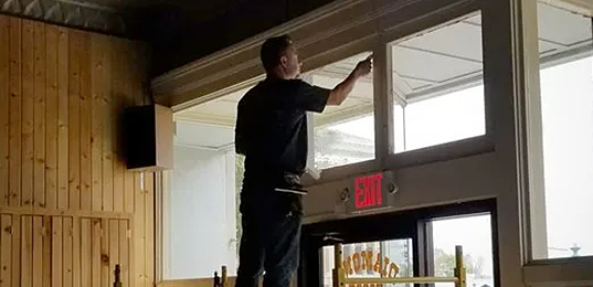 Person adjusting a window in a wood-paneled room above a doorway