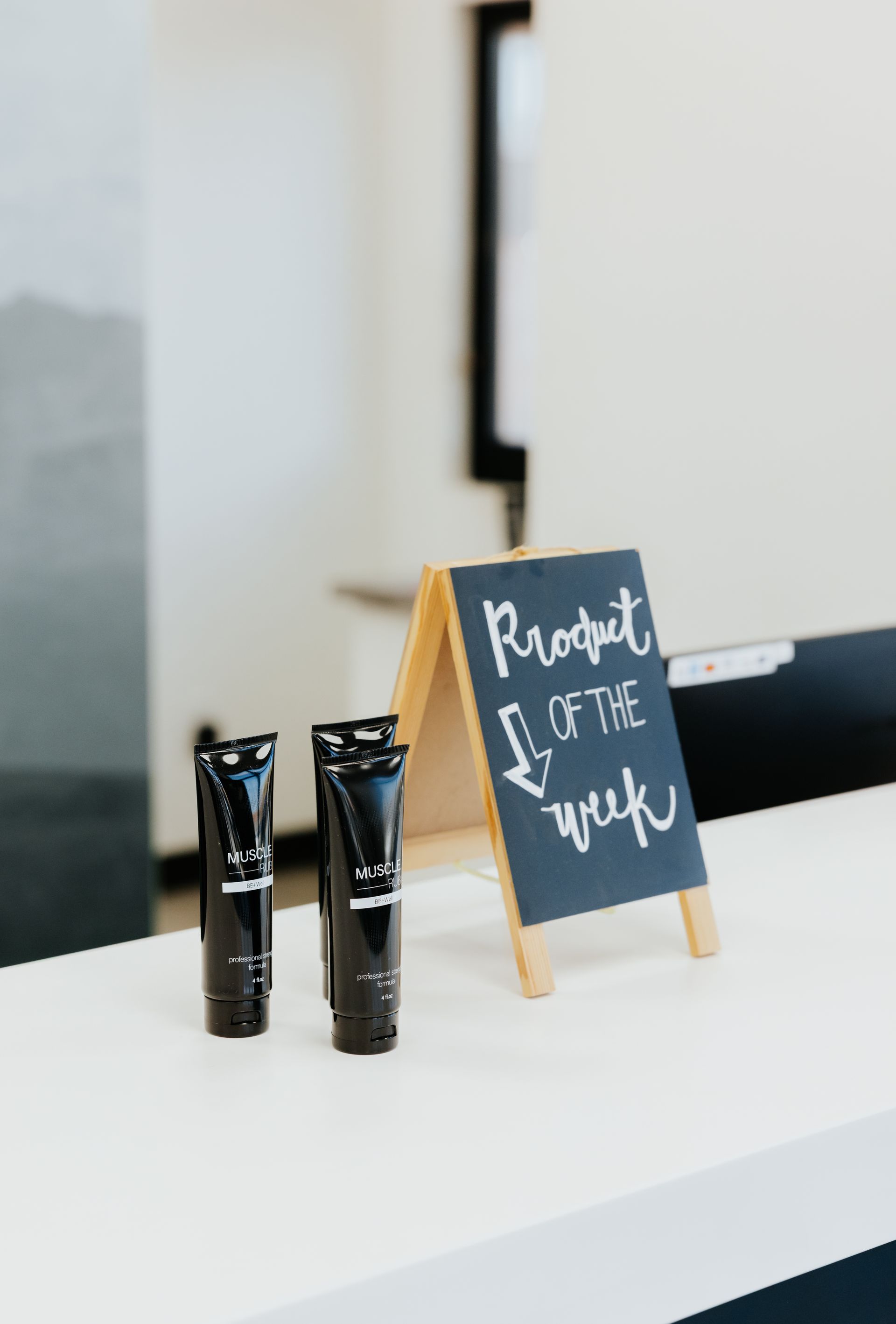 Three black product tubes displayed on a white counter next to a chalkboard sign that says 