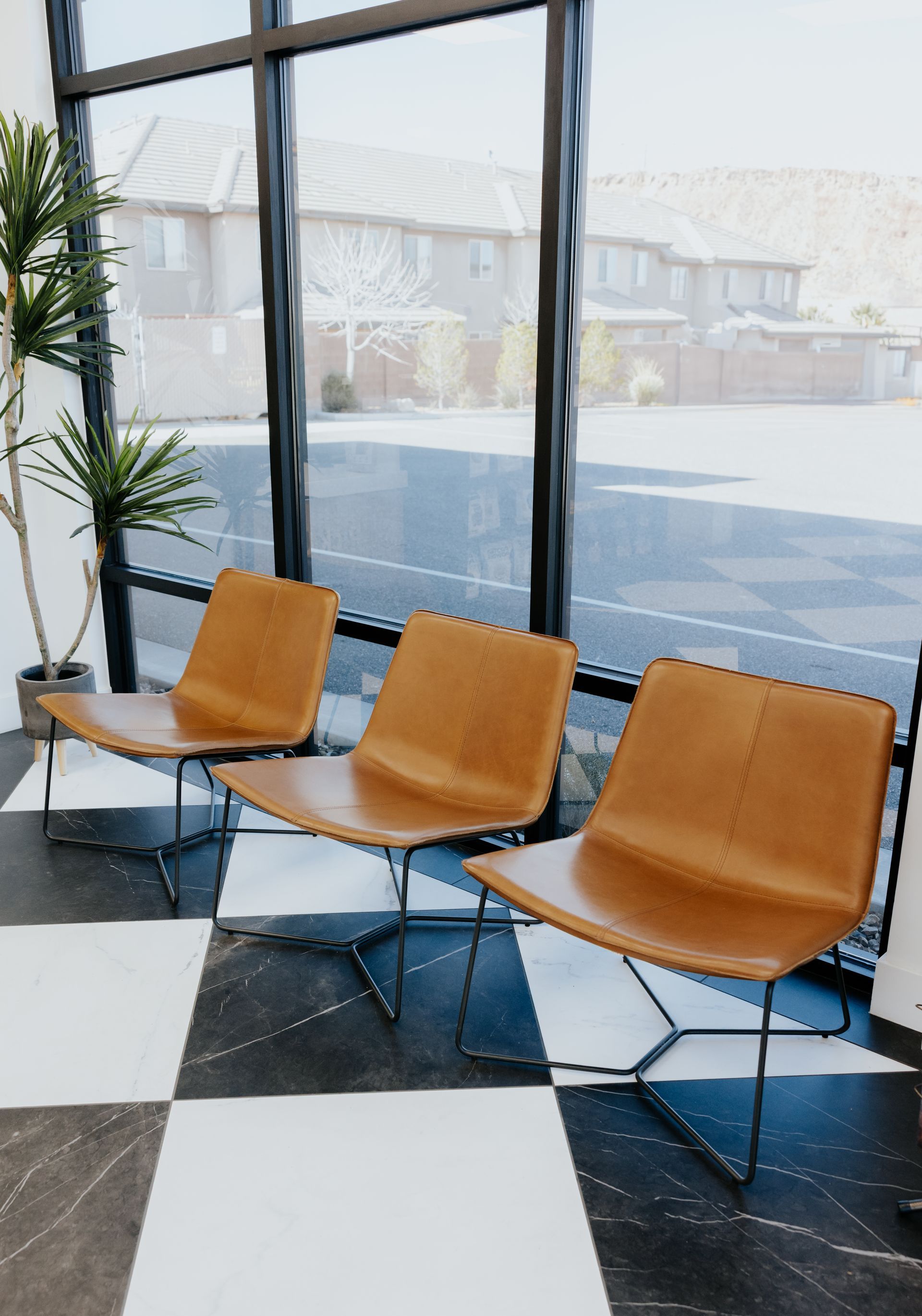 Three tan leather chairs sit in front of a window, on a black and white tiled floor.