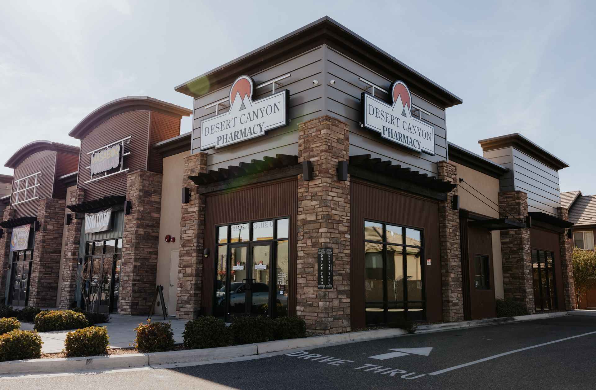 Exterior of Desert Canyons Pharmacy building with signs, stone, and large windows.