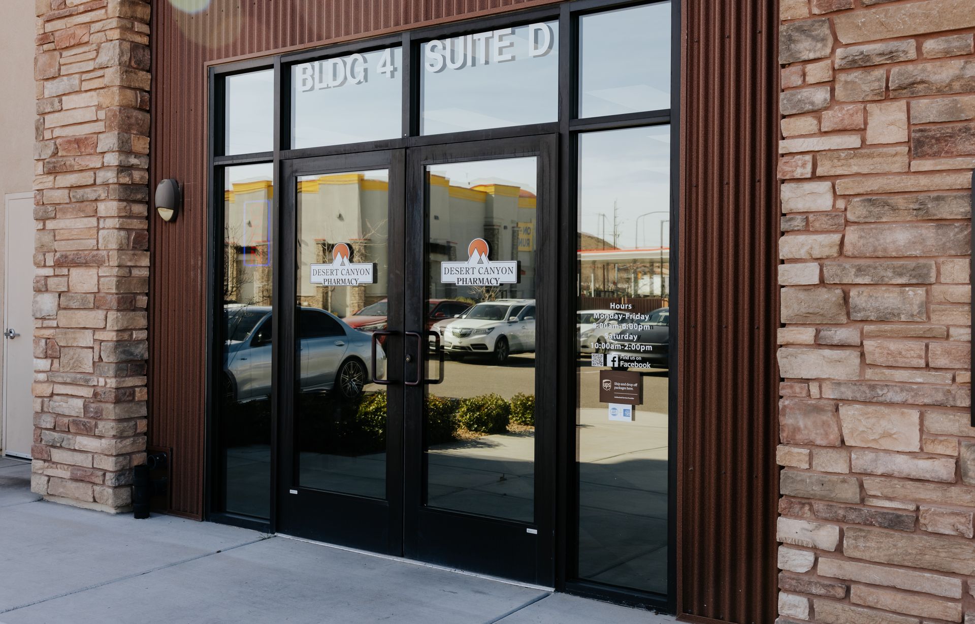 Exterior of a business with glass doors reflecting parked cars and other buildings. Brown brick and paneling around the entrance.
