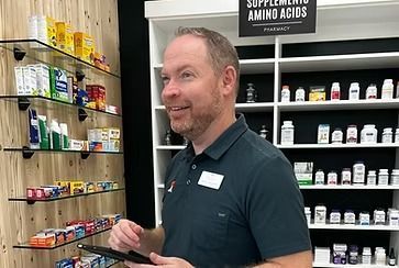 Man in a store with shelves of supplements, smiling and holding a tablet.