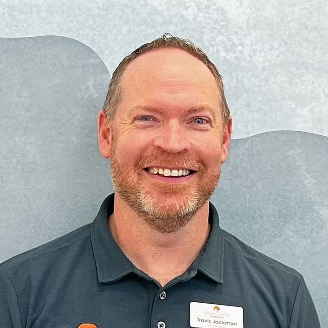Smiling man with short hair and beard wearing a teal collared shirt with a name tag.