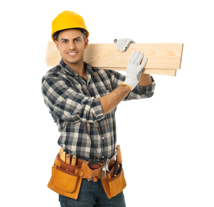 A man wearing a hard hat is carrying a piece of wood.