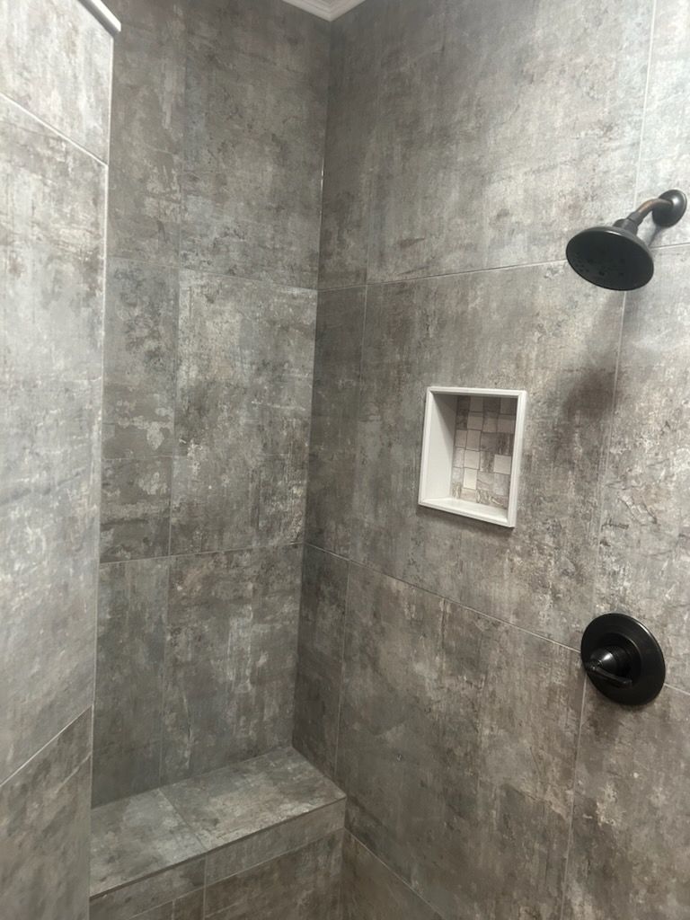 A shower with a gray tile wall and a black shower head.