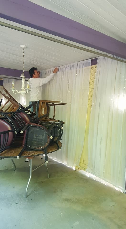 A man is standing on top of a table with chairs in a room.