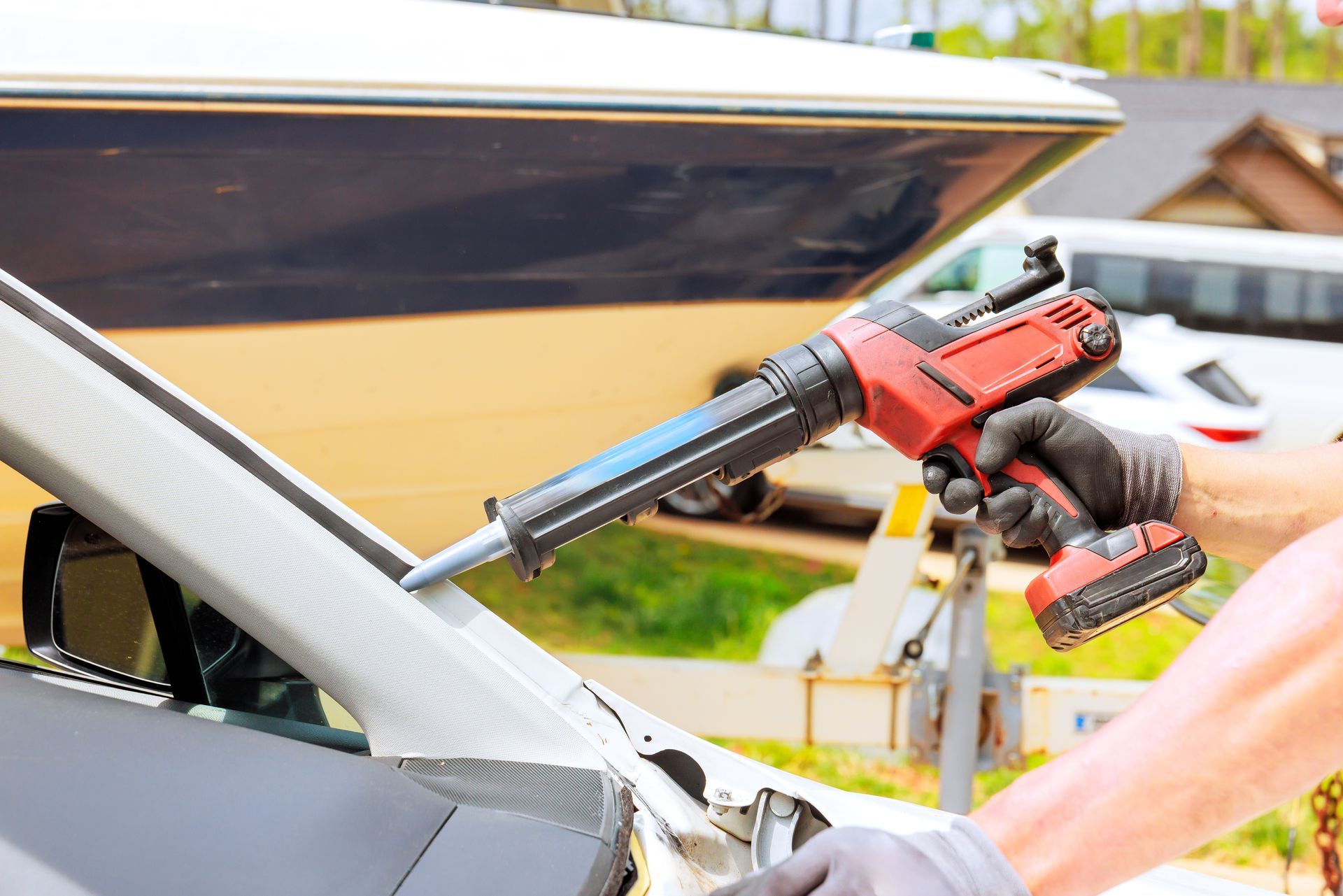 Un ouvrier utilise une perceuse sans fil rouge pour retirer le joint d'étanchéité d'un pare-brise de voiture à l'extérieur.