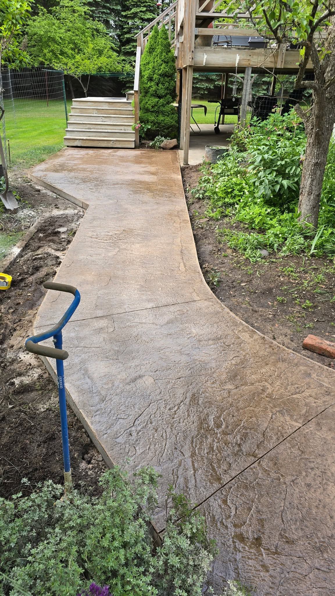 Curved gravel garden path leading uphill past steps, greenery, and a wooden deck.
