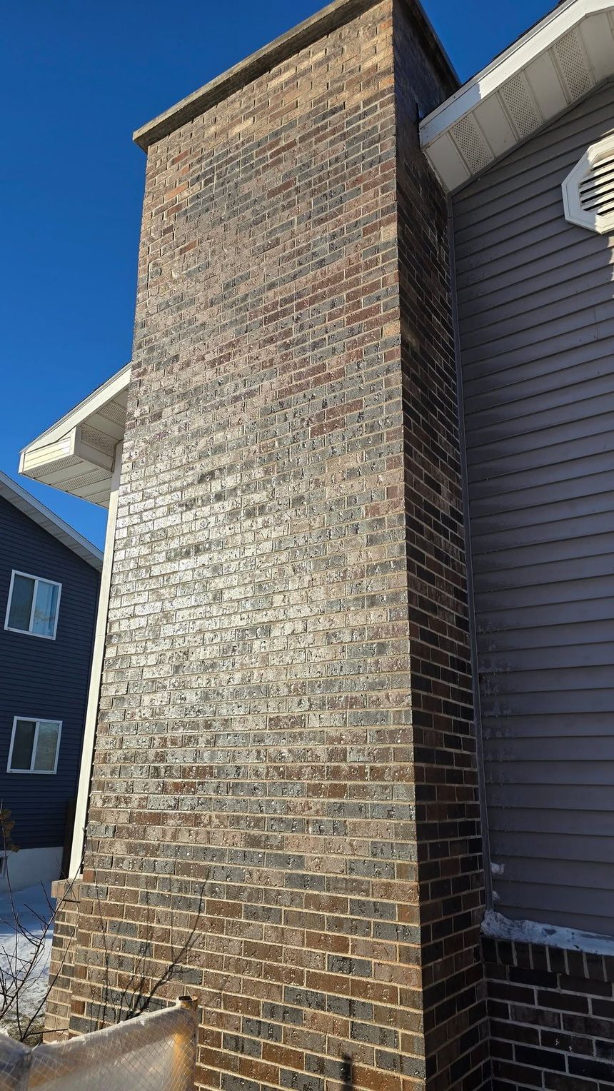 Tall stone chimney beside a gray-sided house under a clear blue sky