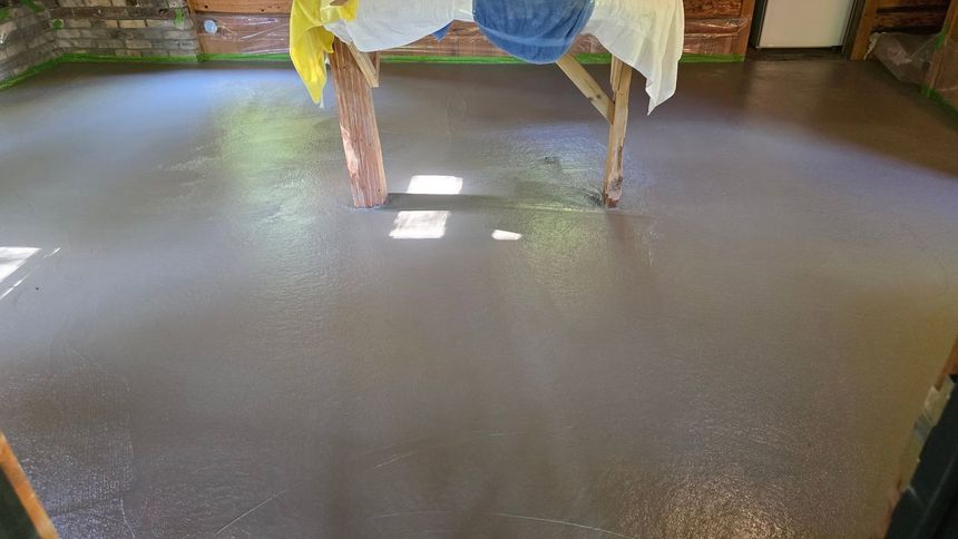 Freshly finished gray floor in a room with covered furniture and sunlight near windows