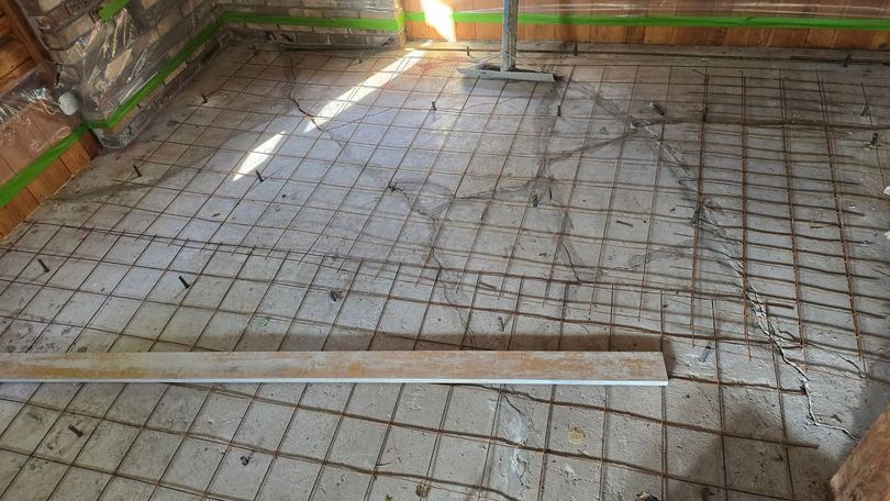 Concrete floor under construction with rebar grid and two metal rails across it