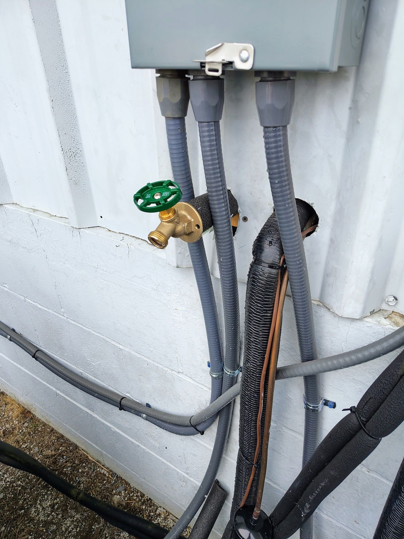 Person kneeling beside a white water heater, inspecting pipes with tools in a utility room.