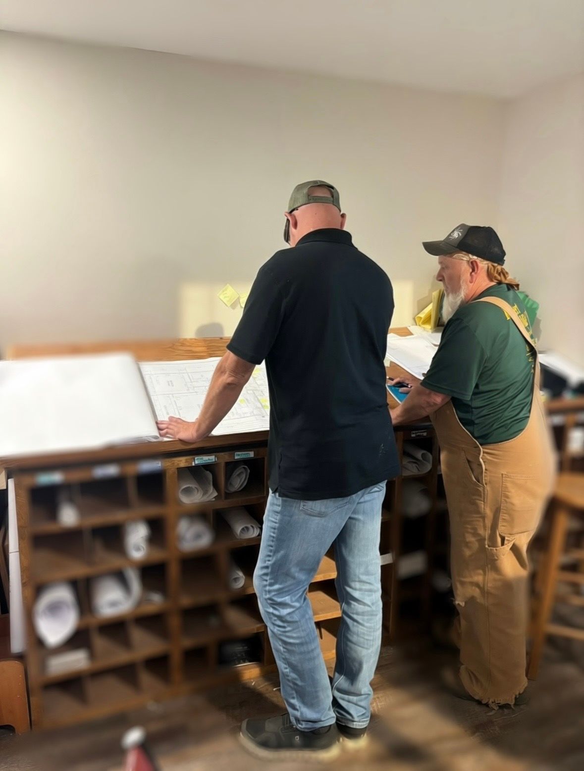 Two people standing at a desk, reviewing papers in a bright room with wooden cubbies.