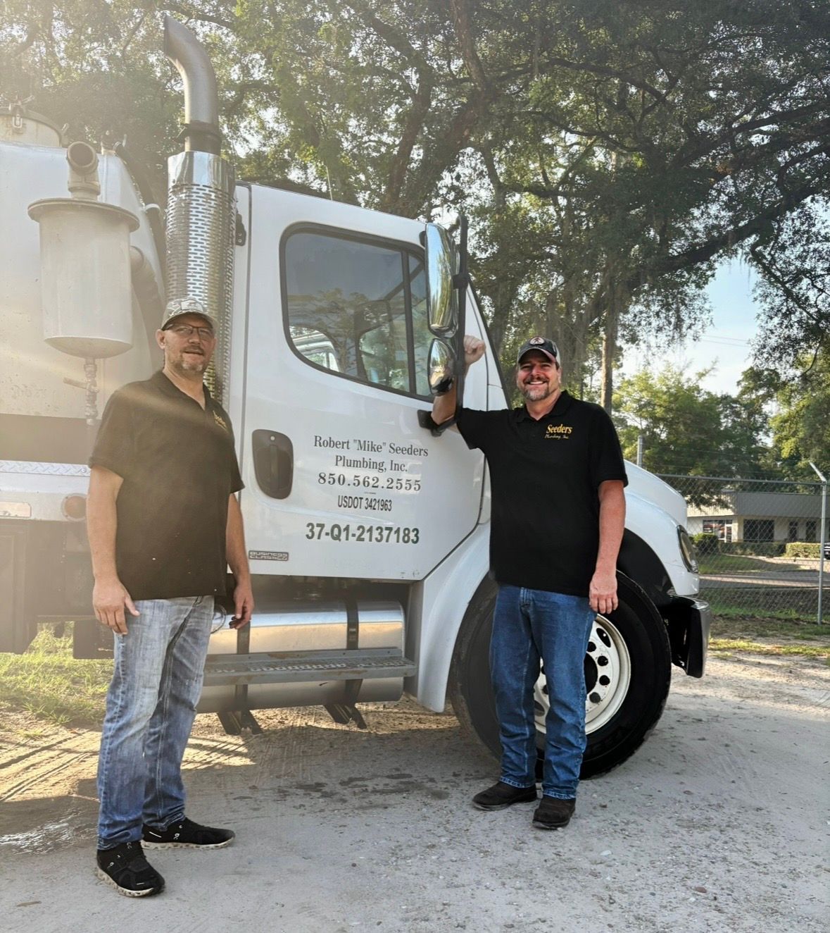Two men standing by a white work truck on a gravel road, one leaning on the open door.