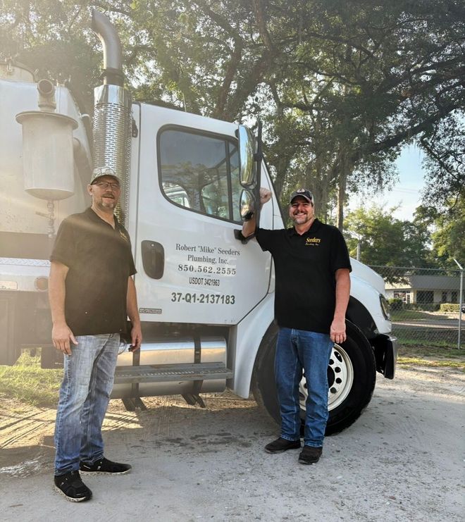 Two men standing beside a white utility truck outdoors, one leaning on the door.